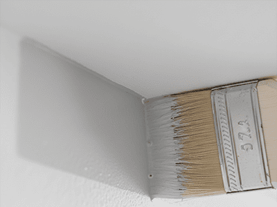 A close-up view of an angled brush creating a perfectly straight paint line on a wall.