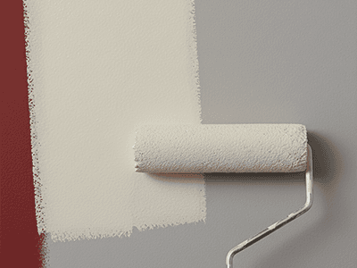 A paint roller applying a light-coloured topcoat over a grey-primed wall.