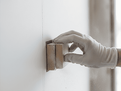 A hand lightly sanding a freshly plastered join on a new gyprock wall.