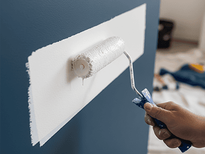 A paint roller applying a high-opacity white primer over a dark coloured wall.