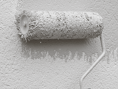 A thick-nap roller applying paint to a textured rendered wall.