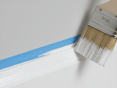 An angled paintbrush applying a smooth coat of white paint to a skirting board.