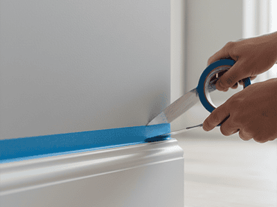 Blue painter's tape being applied neatly along the top of a skirting board.